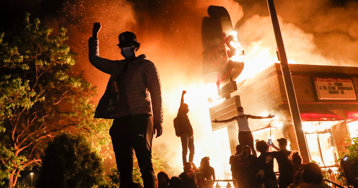 Black lives matter protesters stand outside a burning building. Credit: Getty