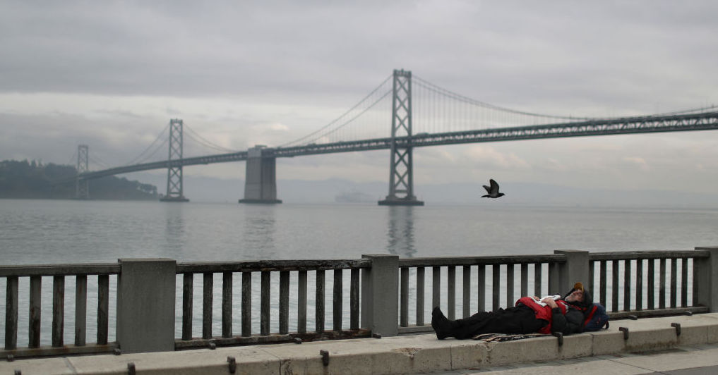 A homeless man sleeps on the sidewalk near the Bay Bridge in San Francisco, California.(Photo by Justin Sullivan/Getty Images)