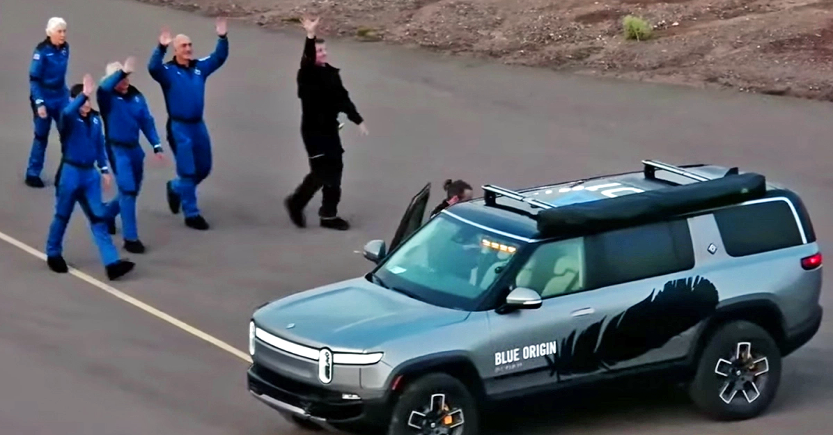 The Blue Origin New Shepard crew, including Jeff Bezos in a cowboy hat, next to Rivian's R1S SUV.
