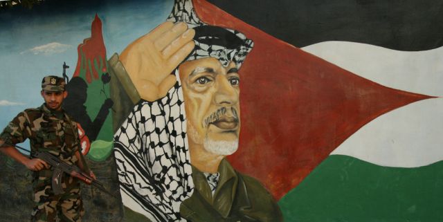 A Palestinian security guard watches over a mural Yasser Arafat (Mahmud HAMS / AFP / Getty)