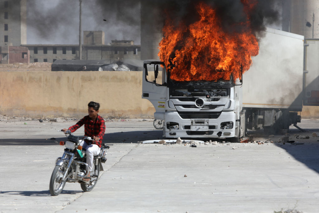 A man rides a motorcycle near a burning Turkish truck during protests in northern Syria this week. Credit: Getty  